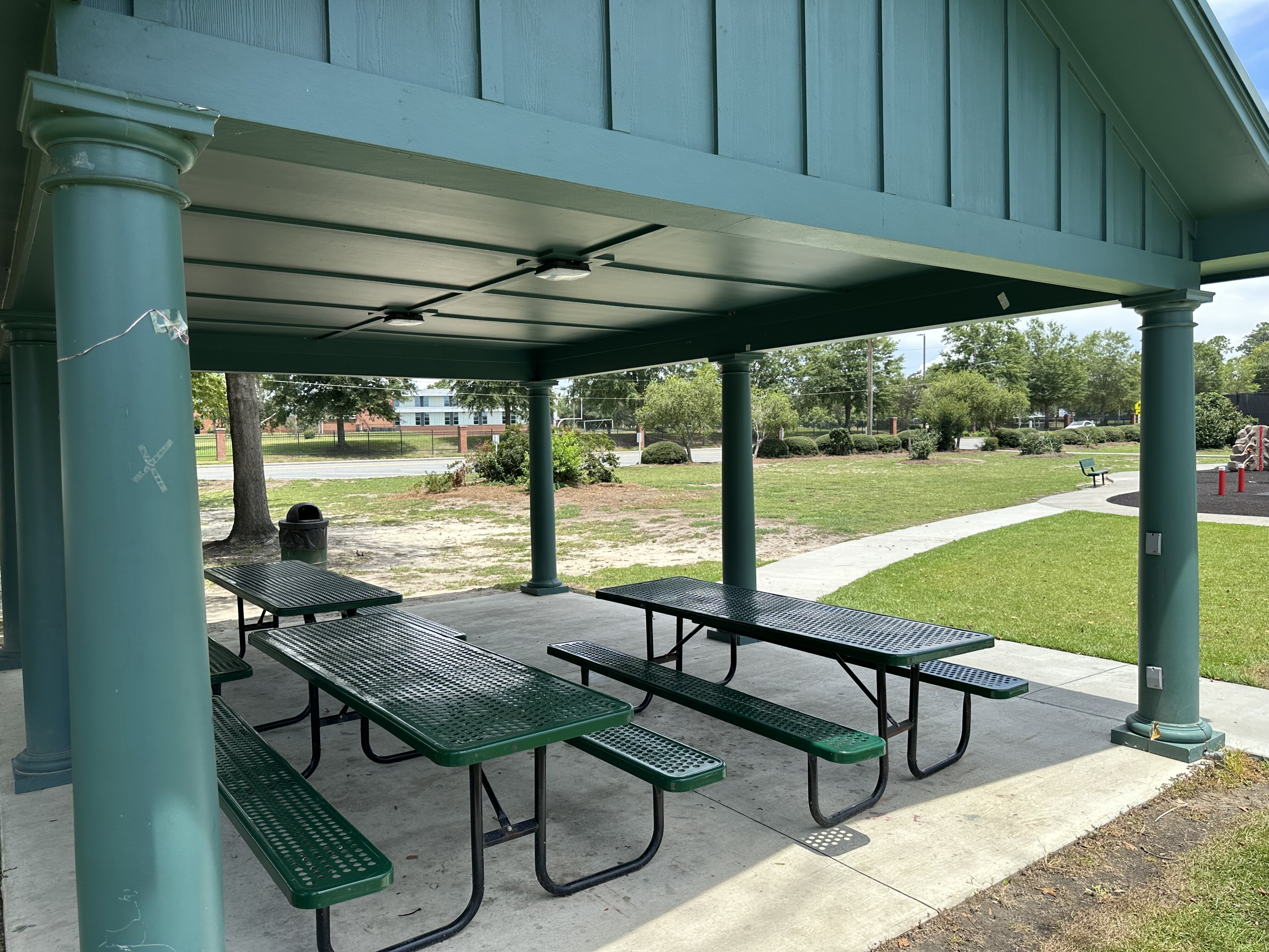 Green metal picnic tables under the open-sided shelter at Mill Pond Park