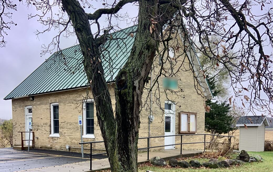 Wrenfield Village Hall, a tan brick building with a green roof, behind a large oak tree